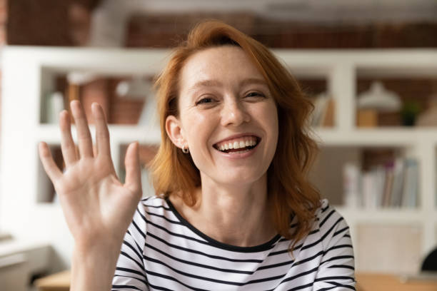 Happy redhead woman greeting friend participate in video conference communication stock photo