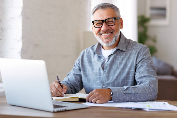 Happy retired pensioner learning studying online on laptop at home stock photo