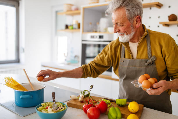 Happy retired senior man cooking in kitchen. Retirement, hobby people concept stock photo