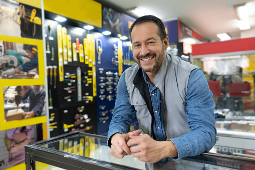 Happy Latin American salesman working behind the counter at a hardware store - small business concepts
