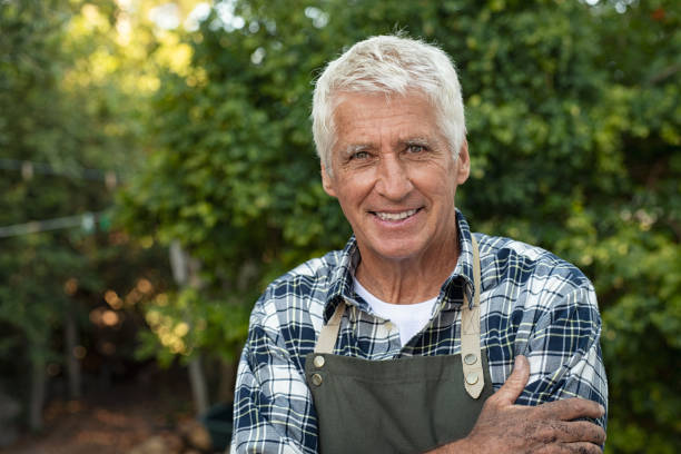 Happy satisfied senior farmer Portrait of happy senior farmer smiling and looking at camera. Cheerful old man with grey hair wearing apron outdoor with copy space. Satisfied smiling gardener in field standing with folded arms. vegetable garden photos stock pictures, royalty-free photos & images