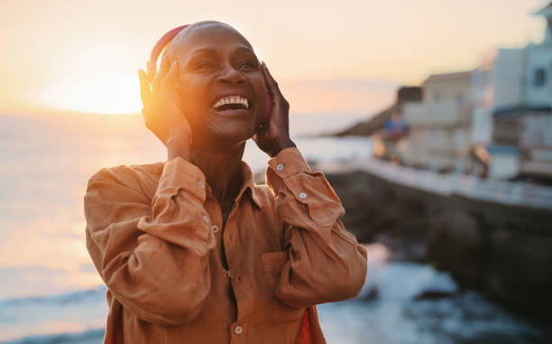lycklig senior afrikansk kvinna njuter av lyssnande musik framför havet under sommarsolnedgången - senior listening music beach bildbanksfoton och bilder