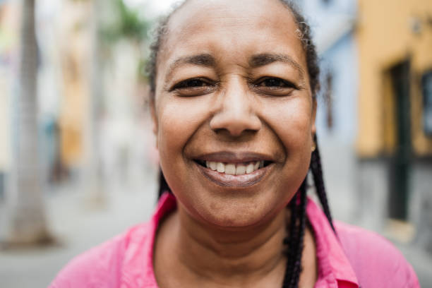 Happy senior african woman posing and smiling on camera with city on background - Real people, diversity and elderly concept - Focus on eyes stock photo