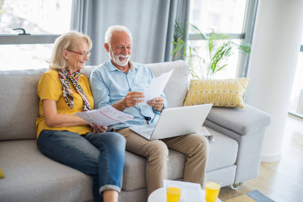 happy senior couple looking at retirement paperwork at home. - hypotheker stockfoto's en -beelden