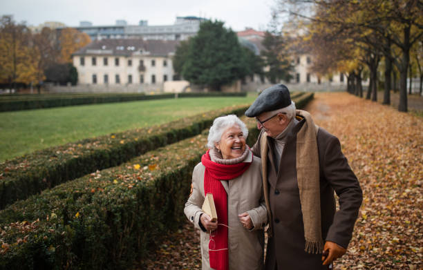 Happy senior couple on walk outdoors in town park in autumn. stock photo