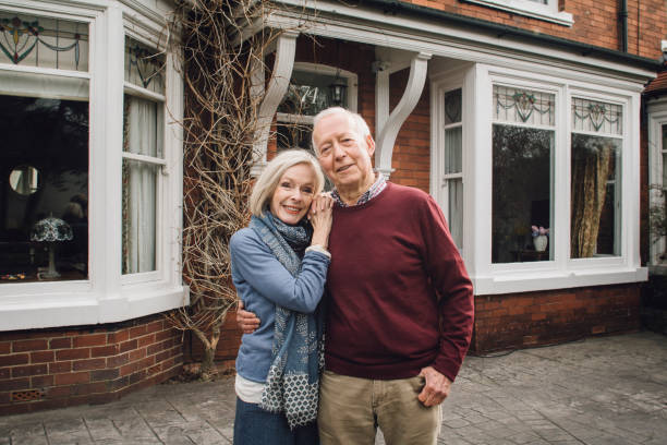 Happy Senior Couple Senior couple are smiling for the camera while standing in front of their home. in front of stock pictures, royalty-free photos & images