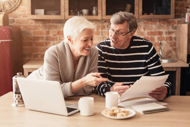 happy senior couple planning family budget junto con laptop and papers - retirement fotografías e imágenes de stock