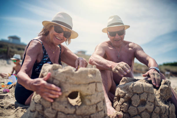 gelukkige senior paar spelen in zand op strand - castle couple stockfoto's en -beelden