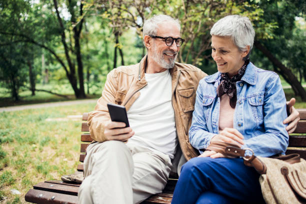 Happy senior couple relaxing in the park and shopping online stock photo