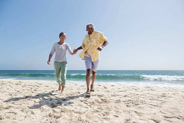 happy senior couple running on the beach - hardlopen vorouw stockfoto's en -beelden