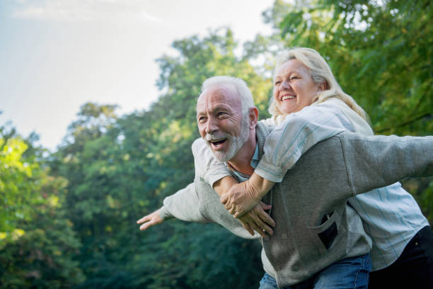 gelukkige senior paar glimlachend buiten in de natuur - piggyback funny stockfoto's en -beelden