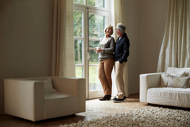 happy senior couple standing by house door - pensioen nederland stockfoto's en -beelden