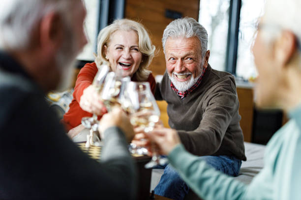 Happy senior couples toasting with white wine at home. stock photo
