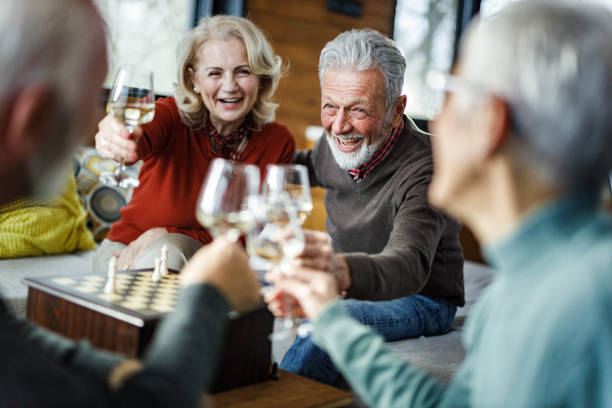 Happy senior couples toasting with white wine at home. stock photo