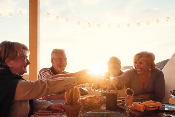 gelukkige hogere vrienden die en rode wijn op huisterras dineren drinken - rijpe mensen die pret hebben die samen bij dinerpartij op zonsondergangtijd juichen - het concept van de voedsel en de bejaarde vriendschapslevensstijl - sunset dining stockfoto's en -beelden
