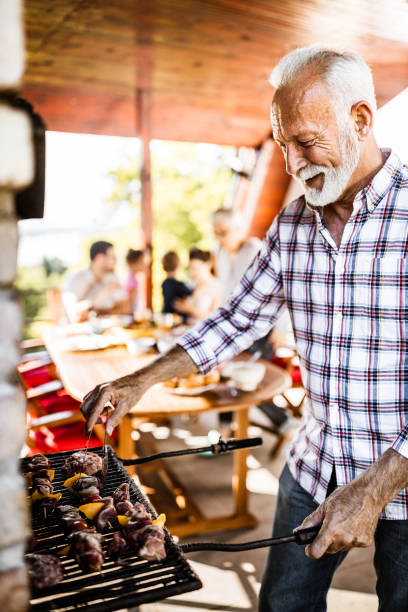 happy senior man making barbecue for his family's lunch on a terrace. - grandparents vertical imagens e fotografias de stock