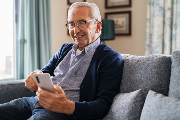 Happy senior man using phone at home stock photo