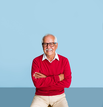 A happy senior latin man with his arms crossed, wearing eyeglasses and smiling at the camera.