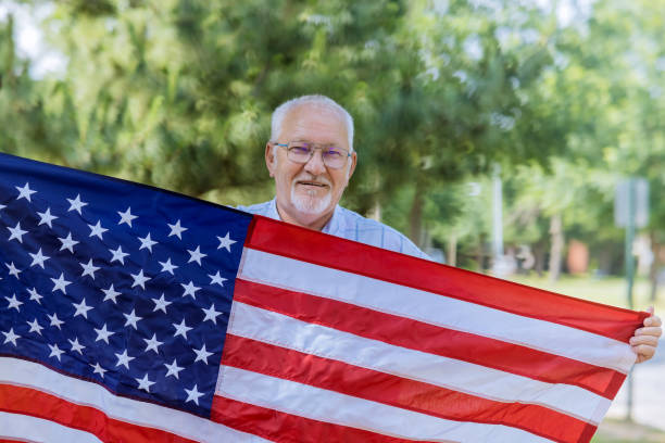 A happy senior patriot wearing a stars and stripes a large American flag. stock photo