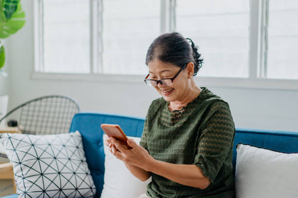 Happy senior woman using smartphone at home Image of a smile senior Asian Chinese woman using smartphone at home asian woman using phone stock pictures, royalty-free photos & images