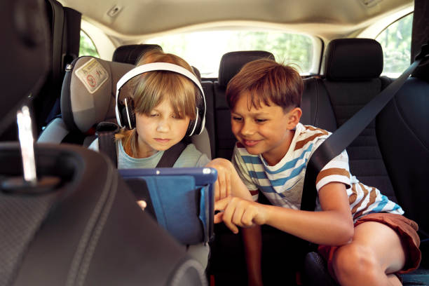 Happy siblings on rear seat of car with tablet stock photo