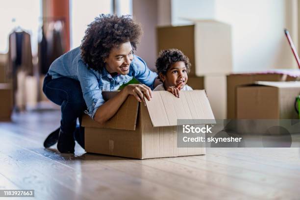 Happy single black mother having fun with her daughter in carton box at new apartment.