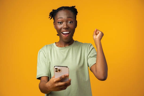 Happy smiling african american girl using her smartphone in yellow studio. stock photo