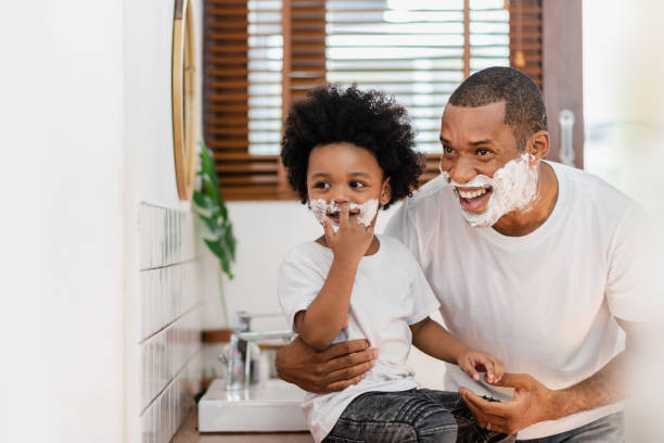 Happy Smiling Black African American Father and little son with shaving foam on their faces having fun and looking away stock photo