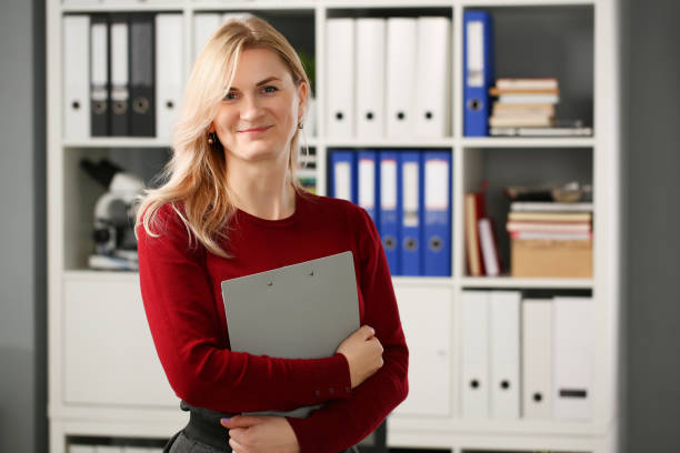 Happy smiling blond businesswoman holdig Happy smiling blond businesswoman holdig gray folder in hand office workplace look at camera administrator stock pictures, royalty-free photos & images