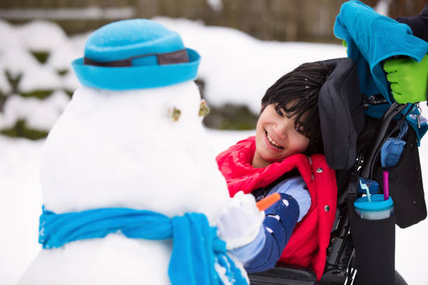 Happy smiling disabled boy in wheelchair building a snowman stock photo