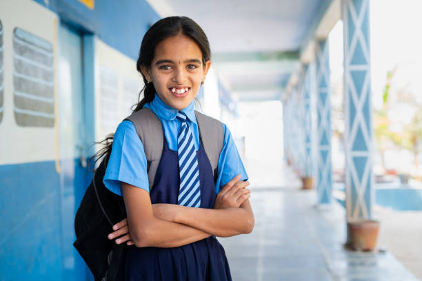 happy smiling girl kid in school uniform confidently standing at corridor with arms crossed by looking at camera - concept of education, knowledge and childhood development - flicka, armar kors bildbanksfoton och bilder