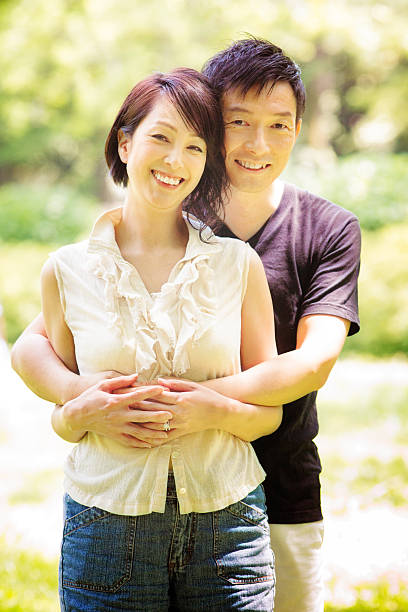 happy smiling healthy mature japanese couple embracing in tokyo park - pregnant couple outside stockfoto's en -beelden