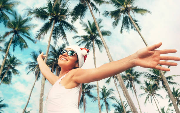 Happy smiling woman in Santa hat stay under palm trees. Christmas holiday on tropical island Happy smiling woman in Santa hat stay under palm trees. Christmas holiday on tropical island exotic asian girls stock pictures, royalty-free photos & images