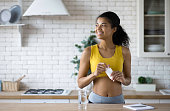 istock Happy sportive african american woman in sportswear holding a bottle of nutritional supplements, looking happily out the window, healthy lifestyle 1323621484