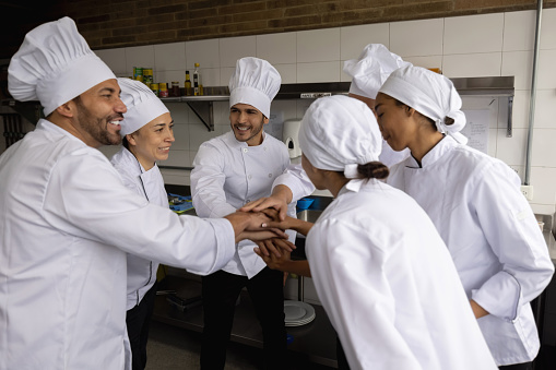 Happy team of chefs in a meeting at a restaurant with hands together and smiling - teamwork concepts
