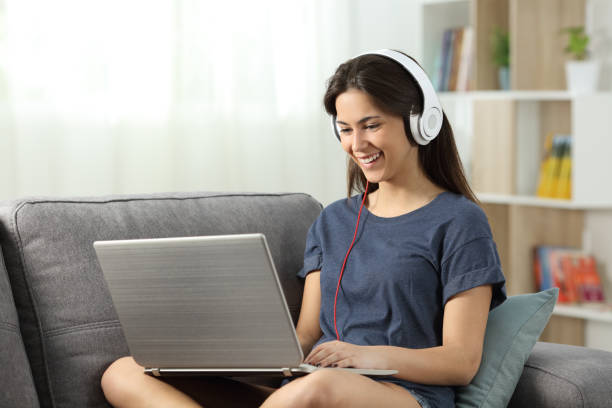 Happy teen watching and listening online content Happy teen watching and listening online content sitting on a couch in the living room at home surfing the net stock pictures, royalty-free photos & images