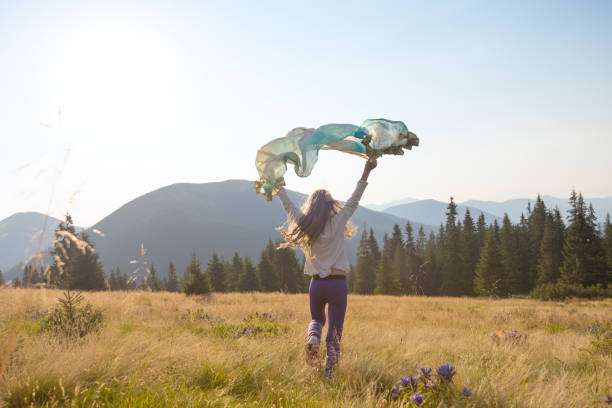 Happy teenage girl runs along the alpine meadow with a waving scarf stock photo