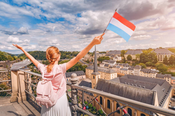 A happy traveller girl holds the flag of Luxembourg and admires the Grund area from the observation deck. Tourism, recreation and life in the country. A happy traveller girl holds the flag of Luxembourg and admires the Grund area from the observation deck. Tourism, recreation and life in the country. luxembourg benelux stock pictures, royalty-free photos & images
