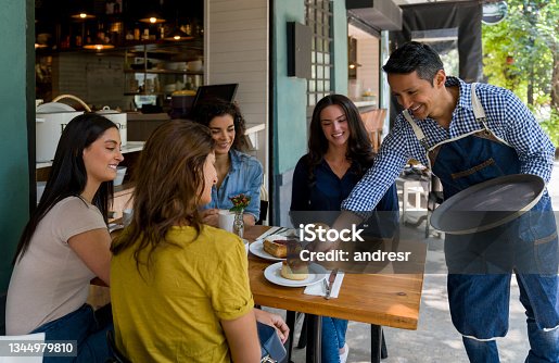 istock Happy waiter serving desserts to a group of women at a cafe 1344979810