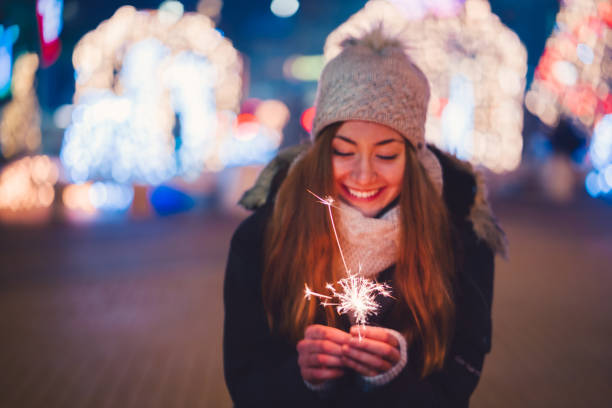 Happy woman at New Year's eve holding burning sparkler Cute girl holding sparkler and enjoying Christmas outside at night new years eve girl stock pictures, royalty-free photos & images