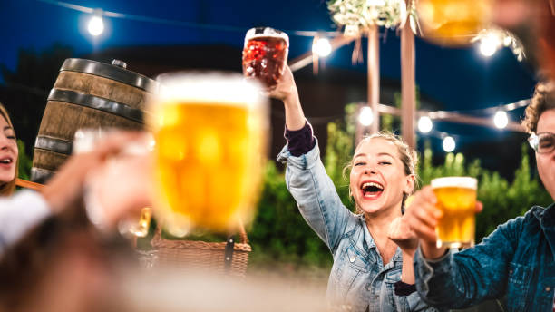 Happy woman clinking and toasting beer at brewery bar restaurant patio with friends - Life style and beverage concept with young people having fun together out side - Focus on face between glasses stock photo