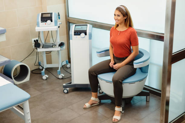 Happy woman during electromagnetic procedure for urinary incontinence at medical clinic. Young happy woman having non-invasive treatment for urinary incontinence at the clinic. pelvic floor stock pictures, royalty-free photos & images