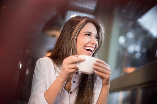 Happy woman having a cup of coffee at a cafe and laughing