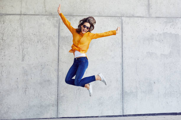Happy woman jumping against concrete wall in the city stock photo
