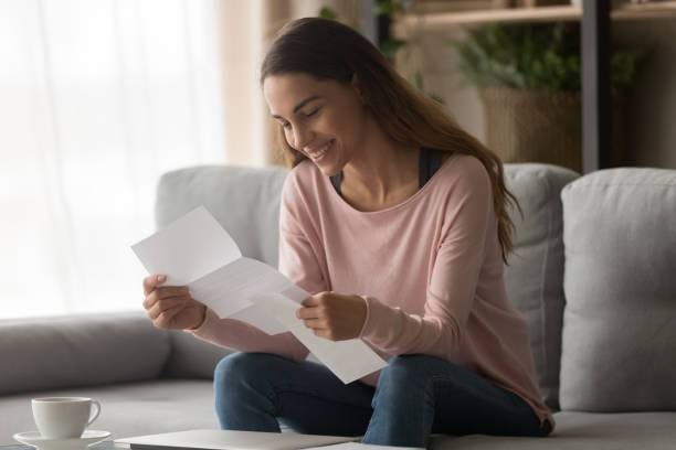 Happy woman read letter with loan approval sit on sofa Happy smiling young woman student customer holding paper bank statement open read mail letter with good news, loan approval, receive scholarship admission money tax refund concept sit on sofa at home scholarships for females stock pictures, royalty-free photos & images