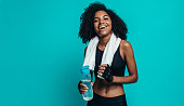 Happy young woman resting after workout on blue background. Healthy young female taking a break after exercising.