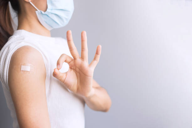Happy Woman showing her arm with bandage and giving ok hand sign after receiving vaccine. Vaccination, immunization, inoculation and Coronavirus ( Covid-19 ) pandemic stock photo
