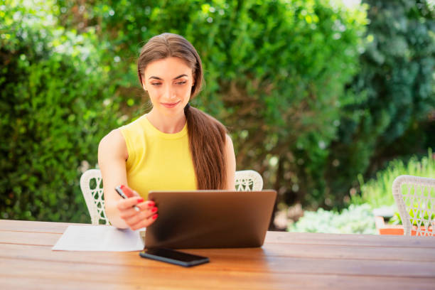 Happy woman sitting at home in the backyard and using laptop while having video call stock photo