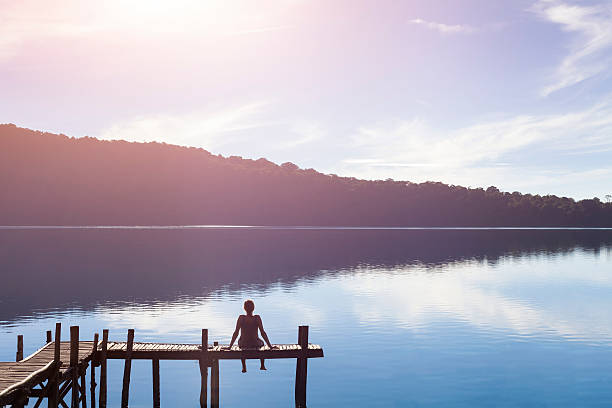 happy woman sitting on a pier getting inspired by nature - rustige scène stockfoto's en -beelden