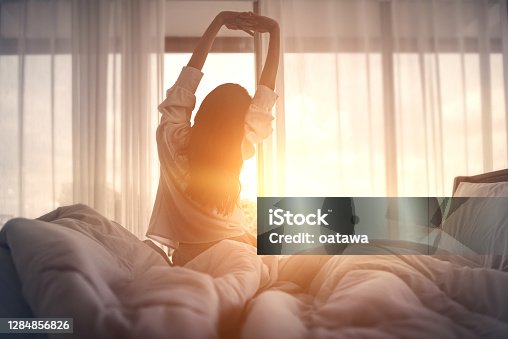 istock Happy woman stretching in bed after waking up. Happy young girl greets good day. 1284856826